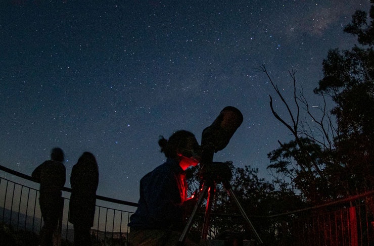 A person peering through a telescope on a starry night.